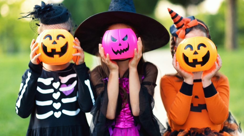 Children in costumes holding up Halloween candy buckets